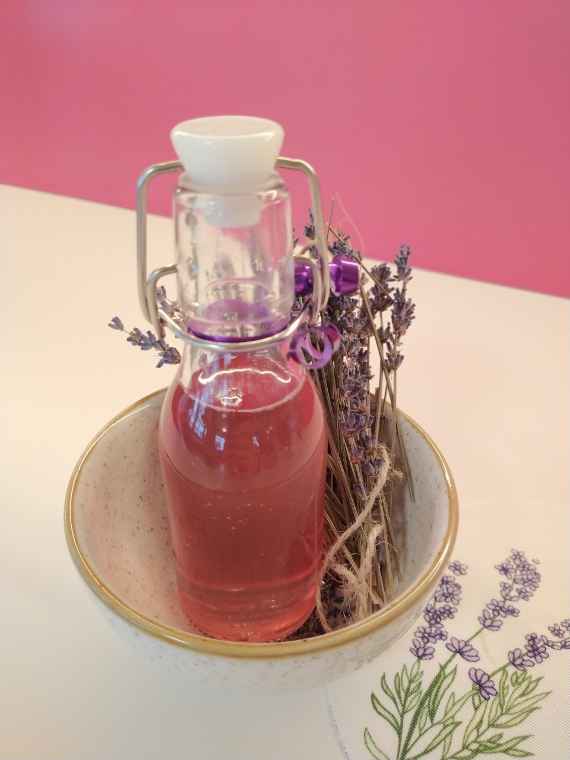 Eine Flasche Lavendelsirup liegt in einer Schale mit Lavendelsträußen. 