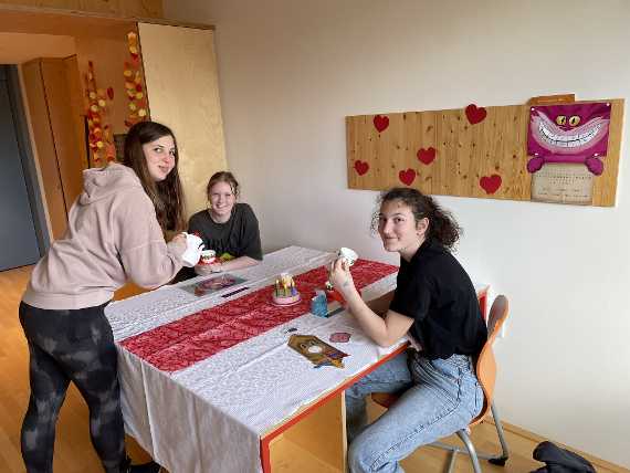 3 Schülerinnen sitzen am Tisch und schauen in die Kamera