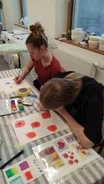 Zwei Schülerinnen malen mit einem Pinsel in ihrer Hand mit Farbe am Papier