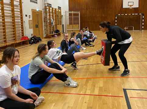 Schülerinnen sitzen am Boden auf Sportmatten und machen Verteidigunsübungen